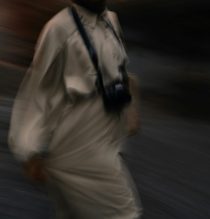 Artistic motion blur photo of a person walking outdoors with a camera.